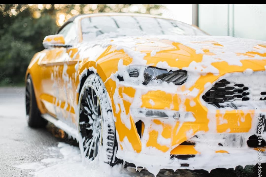 Bright yellow sports car covered in thick white soap suds during a car wash.