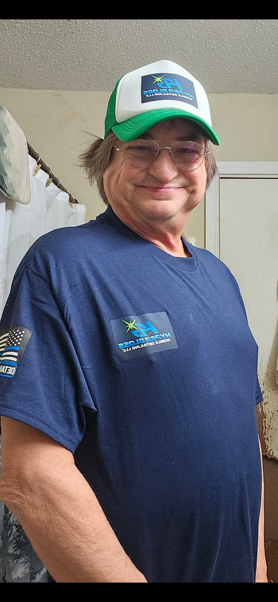 Smiling man wearing a green trucker hat and navy blue t-shirt with company logos.