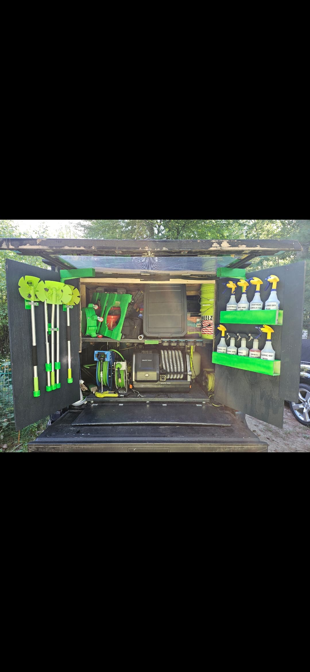 Organized mobile detailing truck bed with neon green tools, spray bottles, and professional cleaning equipment.