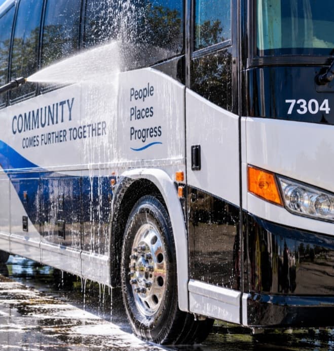 High-pressure water sprays a white community bus featuring the text People Places Progress.