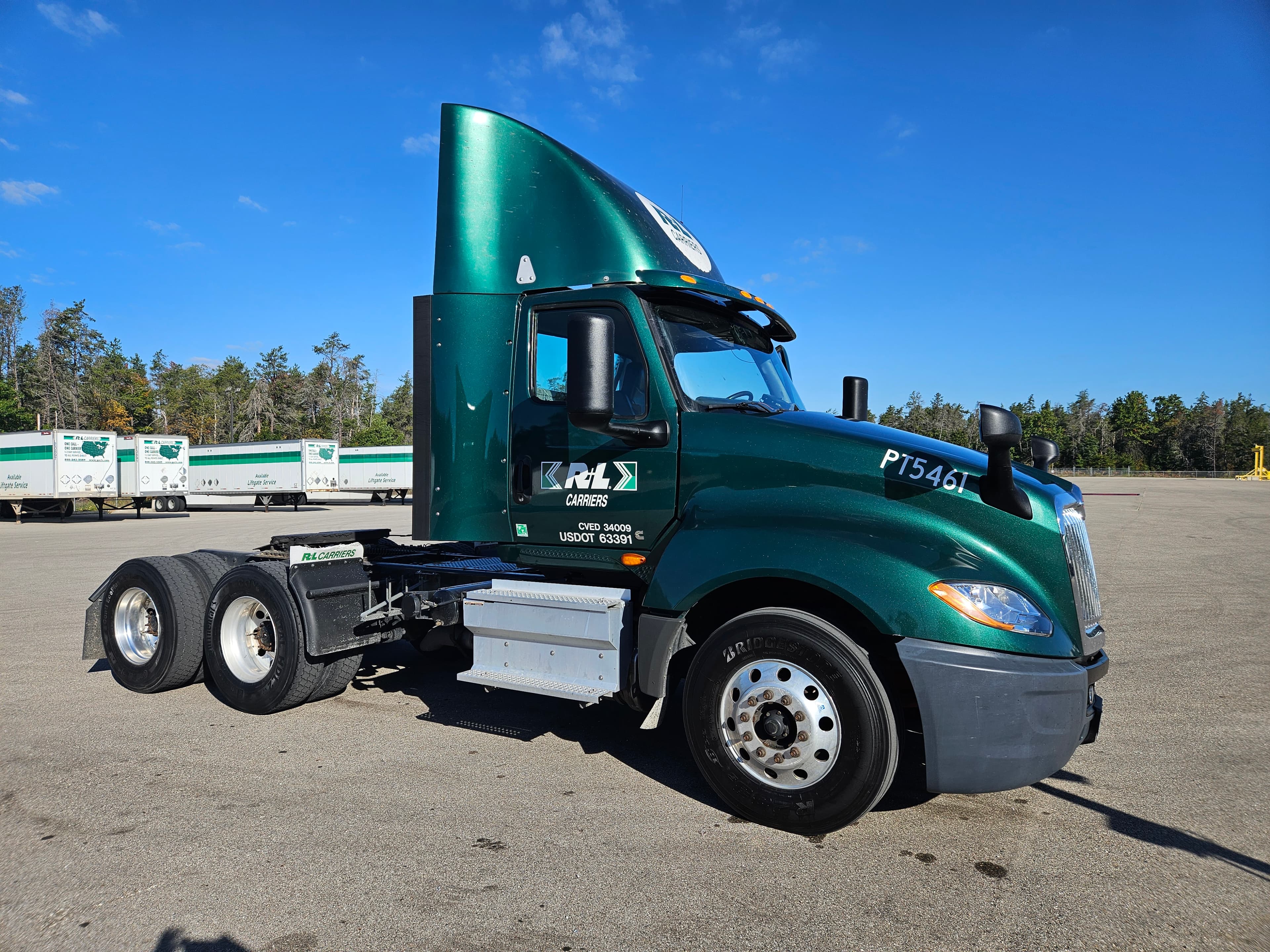 Dark green R+L Carriers semi-truck parked in a lot under a clear blue sky.